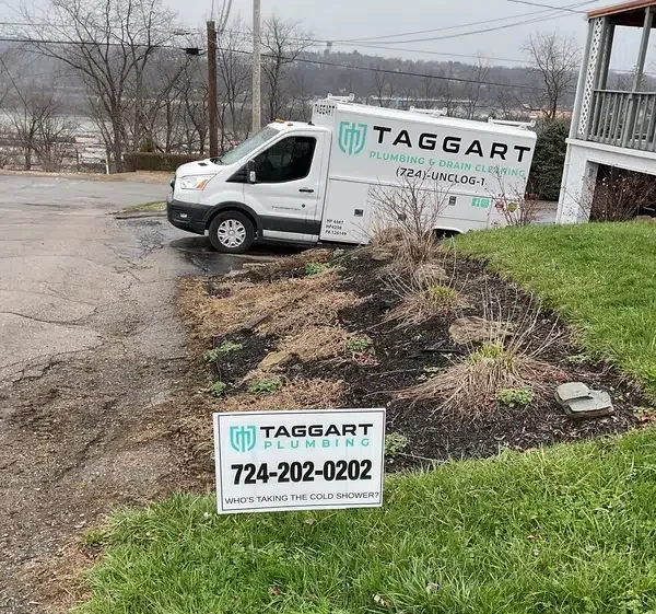 Taggart Plumbing van parked on a residential street with a company yard sign in a front lawn in the Freedom PA area