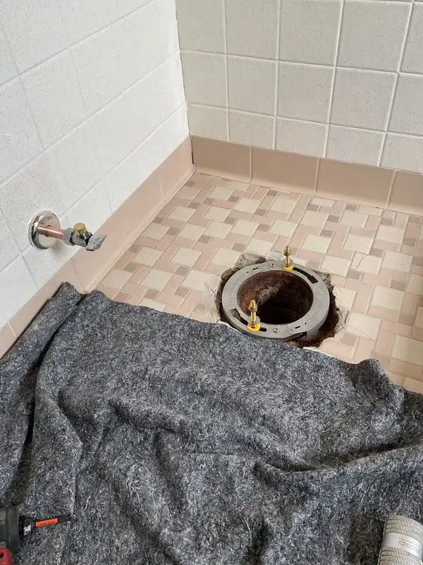 A new toilet flange is installed in the floor and the floor is covered with protective felt or cloth to prevent damage during the renovation.
