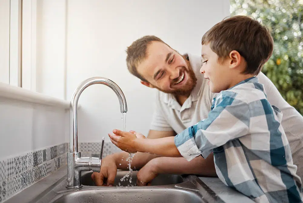 father helping son wash hands in kitchen sink in Pittsburg, PA.