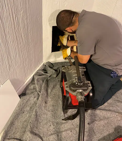 Tech using professional drain cleaning machine with drop cloth to protect floor